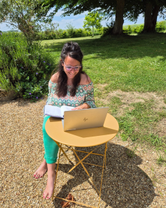 Femme assise dehors au soleil sur une table entrain de travailler avec son ordinateur portable